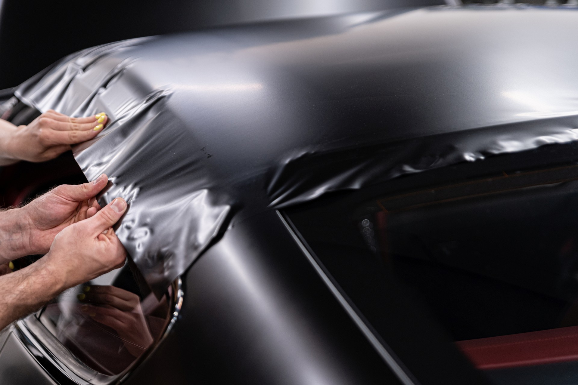 Man worker in car detailing studio applying color changing vinyl foil on car.